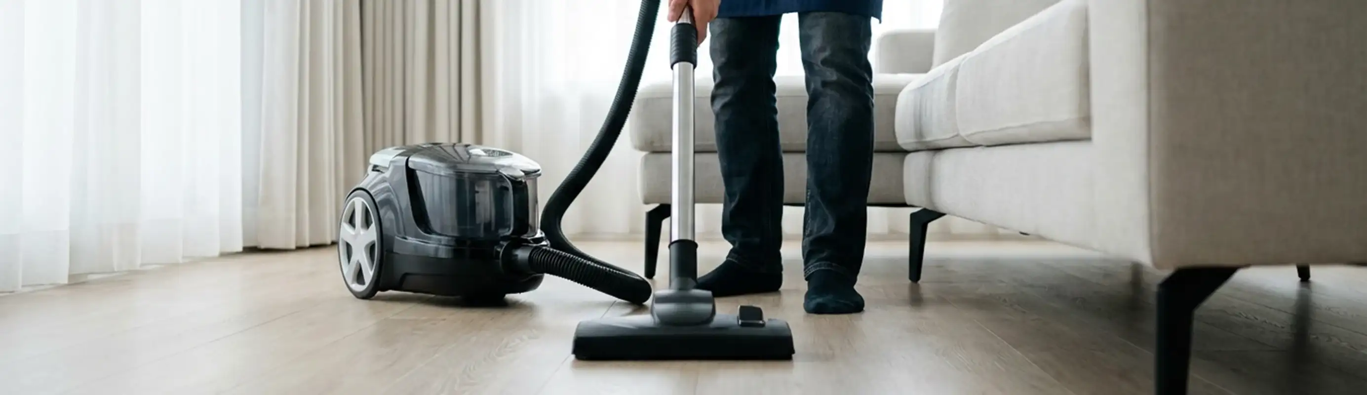 Professional house cleaner vacuuming a living room floor with a canister vacuum cleaner, Mesa, AZ.