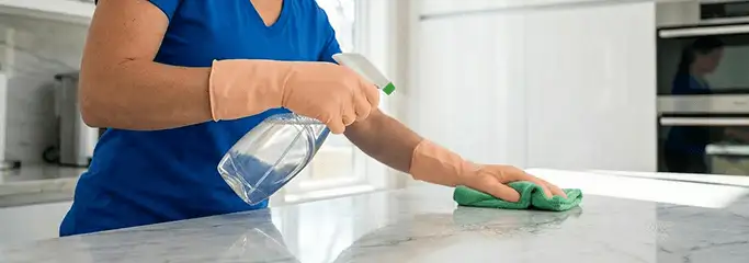 Maid service worker spraying and wiping a kitchen countertop with a microfiber cloth for sanitizing, Mesa, AZ.