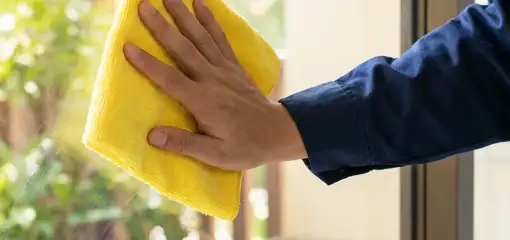 House cleaner wiping a glass window with a yellow microfiber cloth for streak-free cleaning, Mesa, AZ.